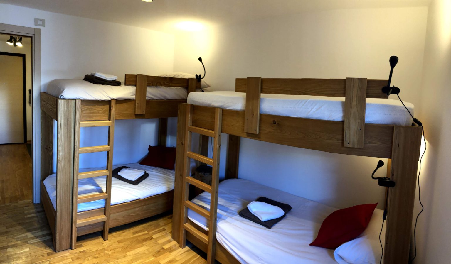 Two wooden bunk beds with white linens, towels, and red pillows in a bedroom with hardwood floors.
