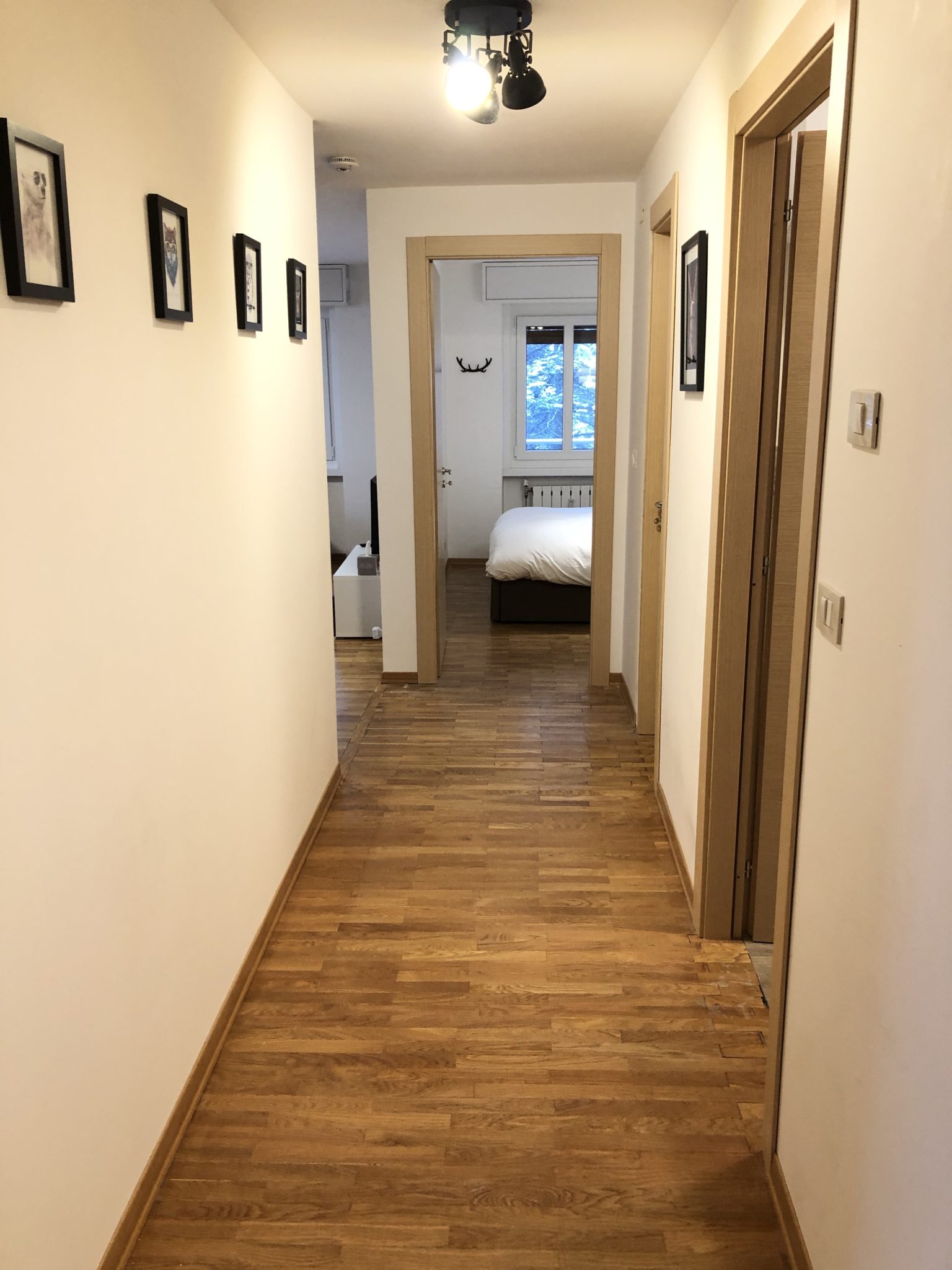 Long apartment hallway with hardwood floors leading toward a bedroom door.