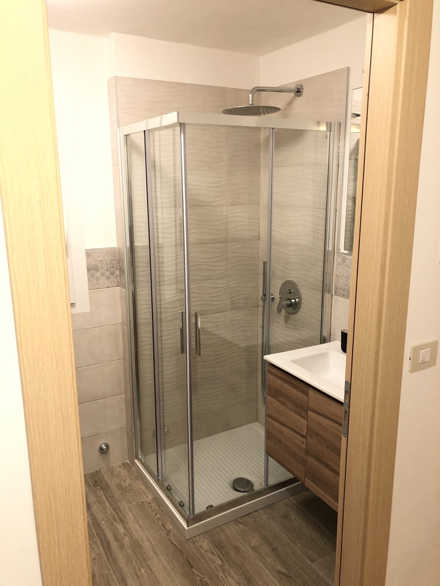 Modern bathroom seen through a doorway, featuring a glass shower stall and a wooden sink vanity.