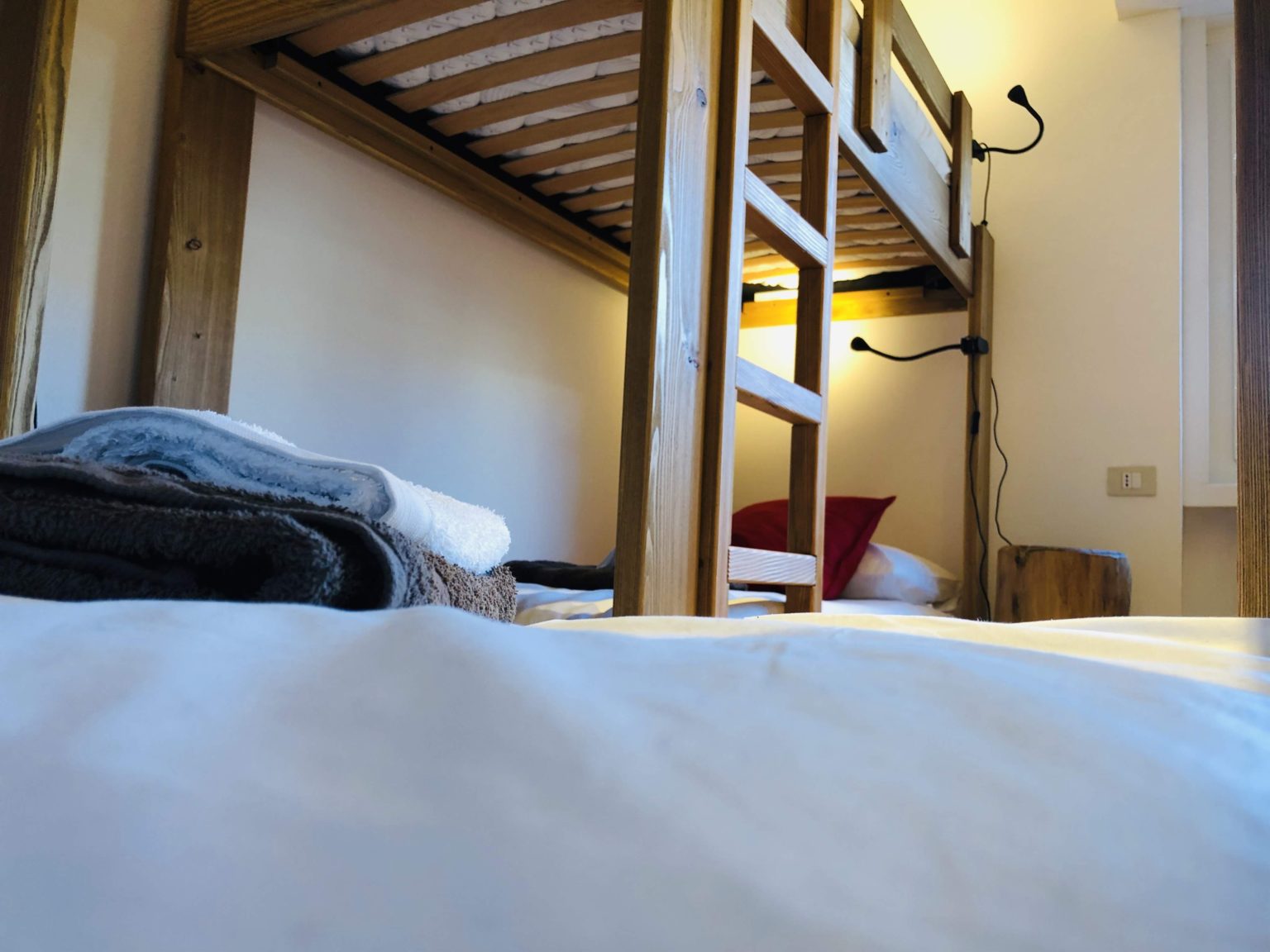 Close-up low angle shot of folded towels on a white bed under a wooden bunk bed frame.
