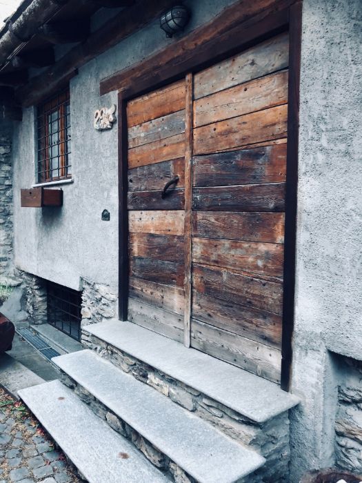 Close-up of a rustic, weathered double wooden door of an old stone building with stone steps leading up.